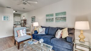 A living room with a blue sofa, a glass coffee table, and a ceiling fan. - Surfside Beach steps away from beach 8/11-8/15; 8/22-8/28; 9/8-9/20; 10/4-10/30 (Surfside Beach)