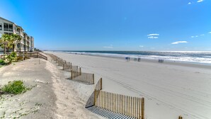 A beach with a wooden fence, a building with balconies, and a clear sky. - Surfside Beach steps away from beach 8/11-8/15; 8/22-8/28; 9/8-9/20; 10/4-10/30 (Surfside Beach)