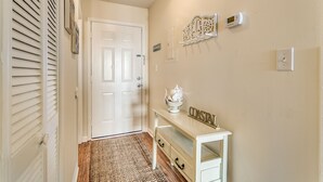 A hallway with a white door, a beige wall, a white console table with drawers, a decorative wall piece, and a thermostat. - Surfside Beach steps away from beach 8/11-8/15; 8/22-8/28; 9/8-9/20; 10/4-10/30 (Surfside Beach)