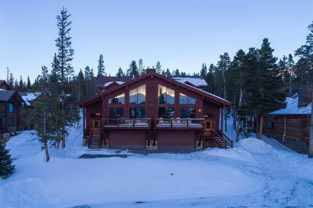 A lodge with a prominent front porch and large windows, surrounded by snow and trees.