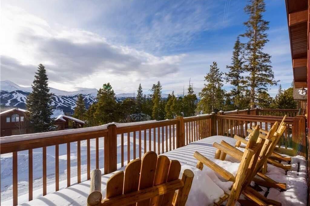 Eine Holzterrasse mit schneebedeckten Stühlen und Blick auf verschneite Berge.