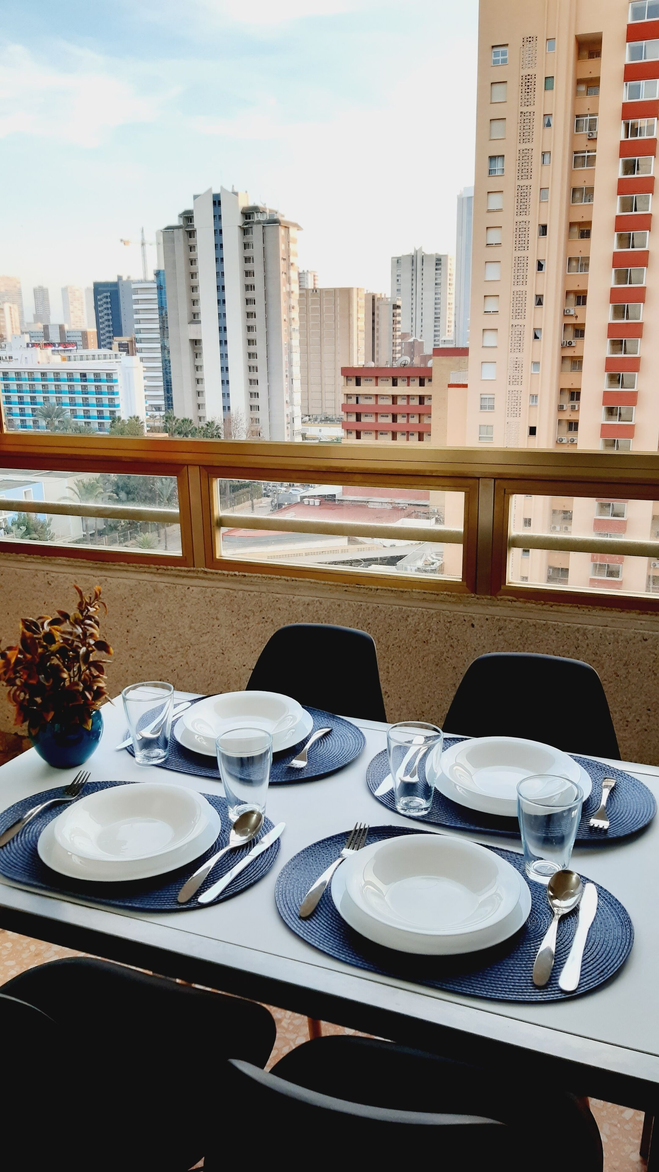 Een eettafel gedekt voor vier personen met uitzicht op de stad, inclusief hoge gebouwen en een weg.
