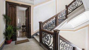 Una maestosa scalinata con ringhiere nere decorate e una balaustra in legno, che conduce a una stanza con una porta in legno e una pianta in vaso.