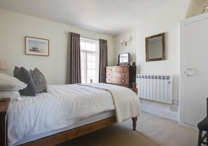 Cozy retreat with a single bed, dresser, TV, and radiator, plus a door to the adjacent space.