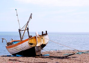 A fishing boat, RACHAEL LIN, is anchored on a pebbly beach, ready for fishing excursions.