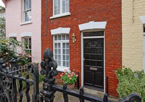 Classic brick house with a traditional black door and white-framed windows, set amidst lush greenery.