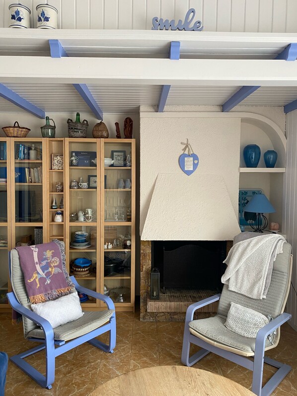 A living room with two blue armchairs, a fireplace, and a bookshelf filled with decorative items. - Mediteranean Sweet & Suite (Palafrugell)