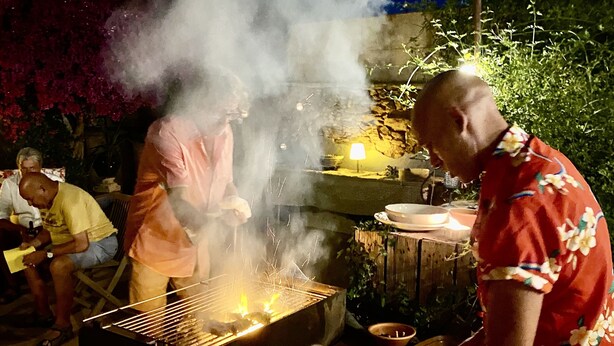 An outdoor barbecue with a grill, food containers, and a person cooking. - Mediteranean Sweet & Suite (Palafrugell)