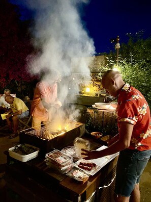 An outdoor barbecue with a grill, food containers, and a person cooking. - Mediteranean Sweet & Suite (Palafrugell)