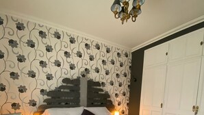A bedroom with a bed, a nightstand, a chair, a chandelier, and a wardrobe. - Mediteranean Sweet & Suite (Palafrugell)