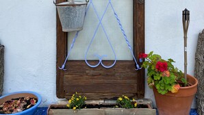 A wooden door with a metal lattice and heart-shaped decorations, a blue bucket, a potted plant with red flowers, and a blue bowl on a tiled floor. - Mediteranean Sweet & Suite (Palafrugell)