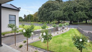 Un edificio moderno con un acceso cubierto, un césped bien cuidado y una hilera de árboles pequeños con flores blancas.