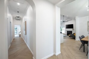 Un interior moderno con un pasillo que conduce a un comedor, una sala de estar con chimenea y un televisor montado en la pared.