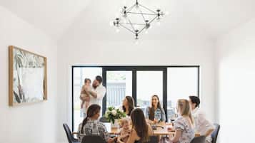 A modern dining area with a geometric chandelier, large windows, and a framed artwork on the wall.