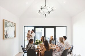 Un comedor moderno con una lámpara de techo geométrica, ventanas amplias y una obra de arte enmarcada en la pared.