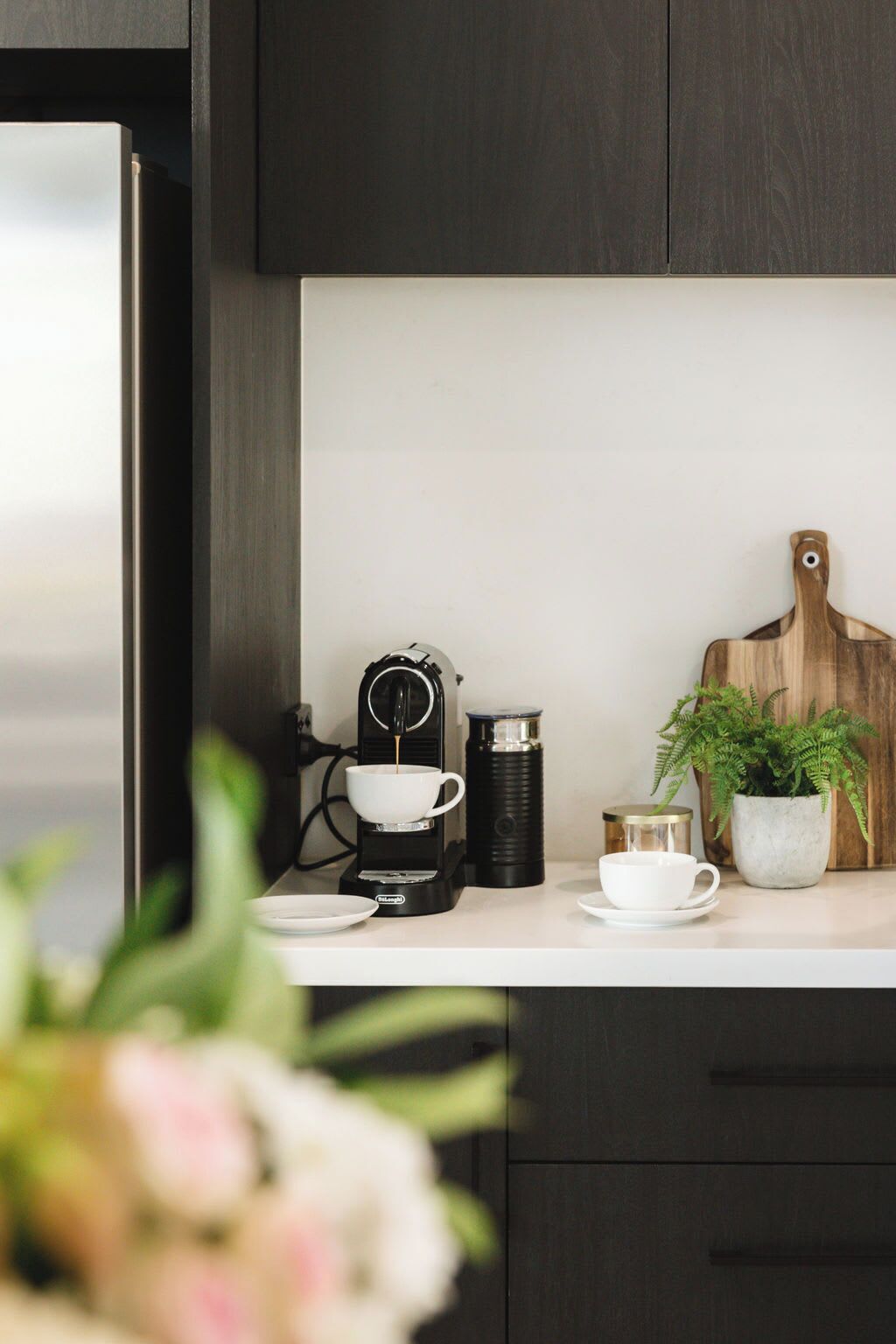 Una encimera de cocina con una cafetera, una taza, un termo, una tabla de cortar y una planta en maceta.