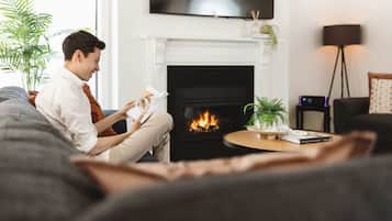 A person sitting on a couch reading a book in a living room with a fireplace, a TV mounted on the wall, and a floor lamp.