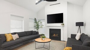 A modern living room with a grey sofa, a round coffee table, a fireplace, a flat-screen TV, and a ceiling fan. - The Abode - Luxury, centrally located, 10 guests. (Mount Gambier)