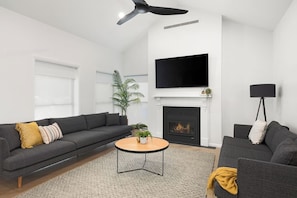 A modern living room with a grey sofa, a round coffee table, a fireplace, a flat-screen TV, and a ceiling fan. - The Abode - Luxury, centrally located, 10 guests. (Mount Gambier)