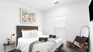 Un dormitorio moderno con una cama grande, una mesita de noche, una silla y una ventana.