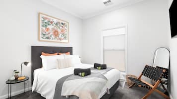 A modern bedroom with a large bed, a side table, a chair, and a window.