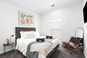 Un dormitorio moderno con una cama grande, una mesita de noche, una silla y una ventana.