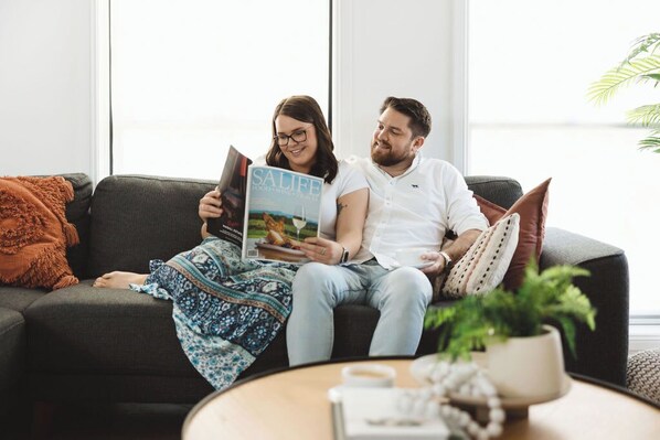 Una pareja sentada en un sofá con una revista, una taza de café y una planta sobre una mesa.