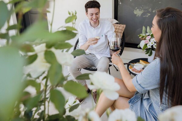 Una pareja sentada en una silla con una mesa entre ellos, sosteniendo una copa de vino tinto y un plato de comida.