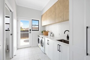 A modern kitchen with white cabinetry, a built-in washing machine, and a herringbone tile backsplash.