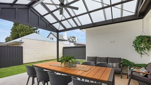 Un porche cubierto con una mesa y sillas de madera, un sofá y plantas en macetas.
