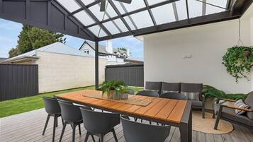 A covered patio with a wooden table and chairs, a sofa, and potted plants.