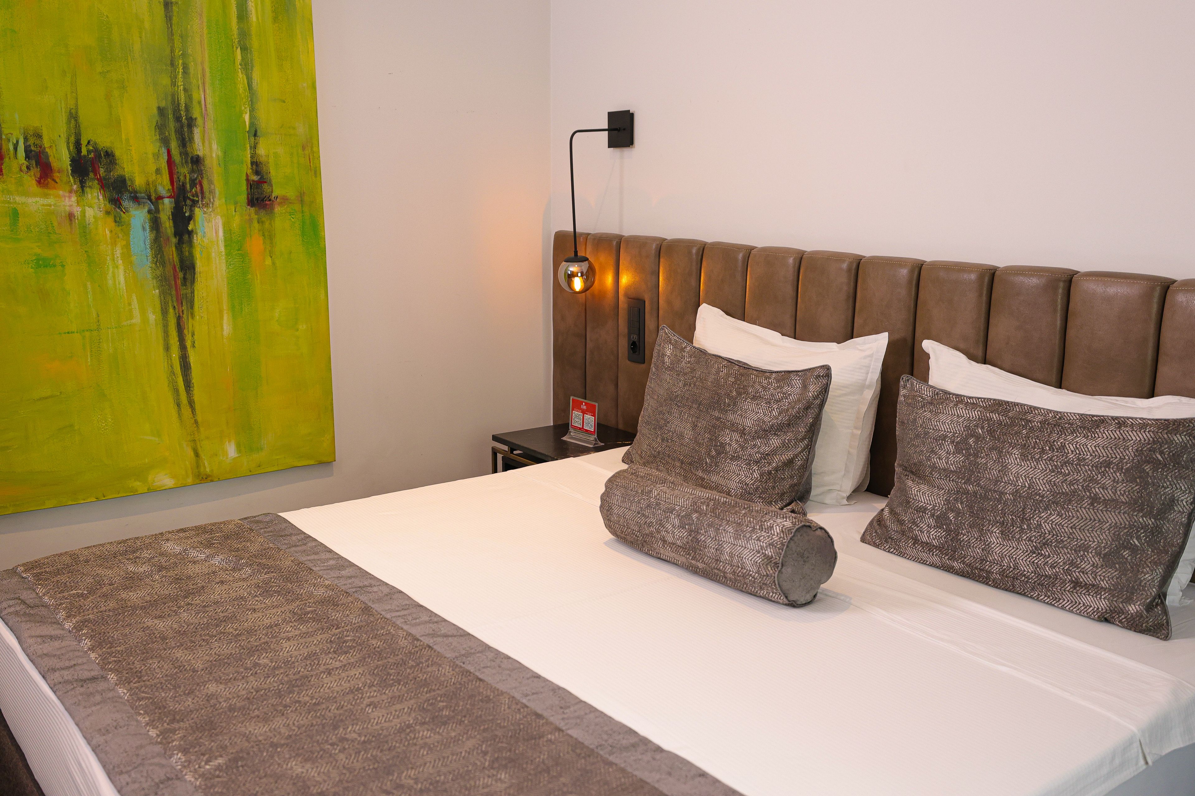 Een netjes opgemaakt bed met een bruin hoofdbord, een geborduurd deken en twee kussens.