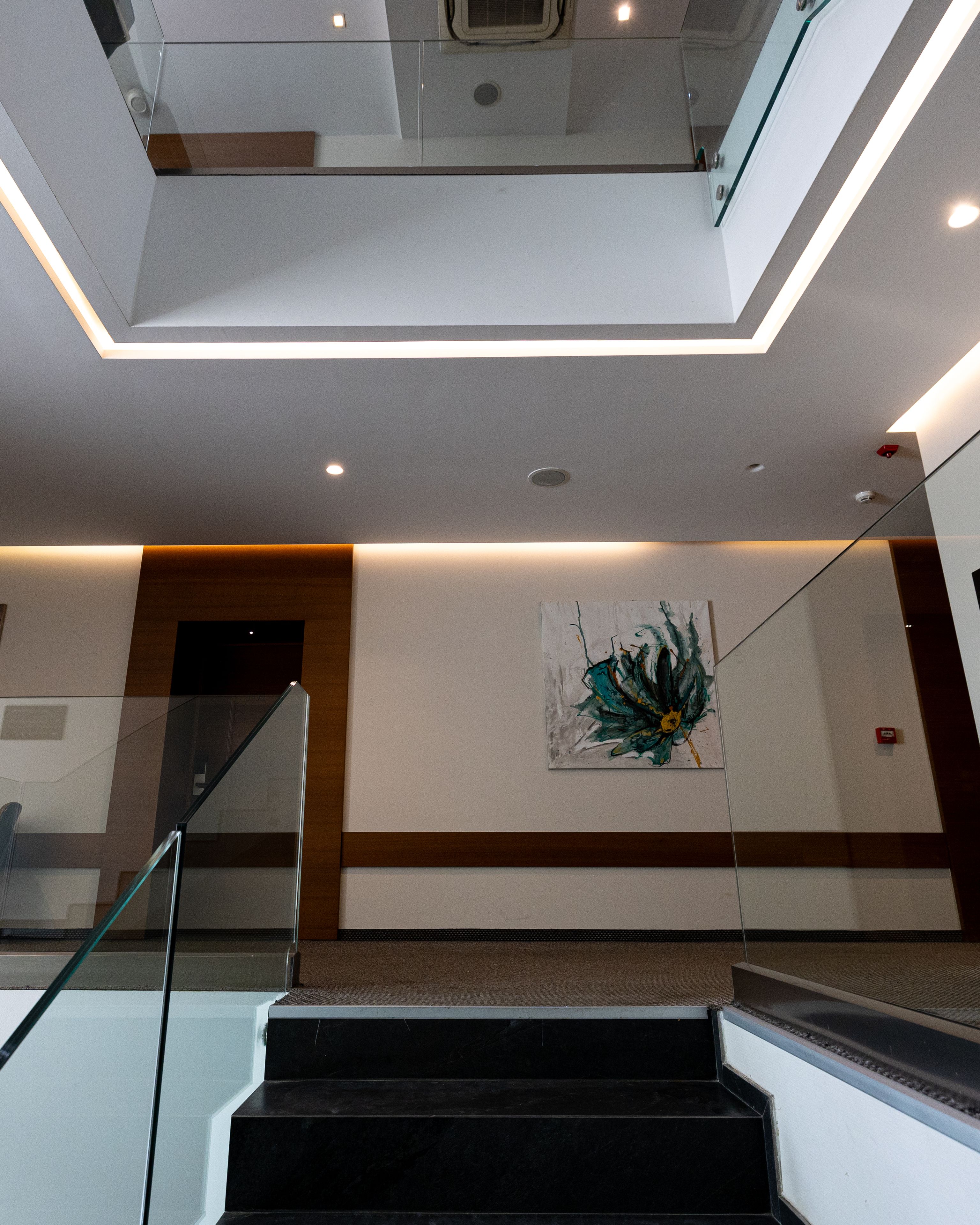 Ein modernes Interieur mit einer Glaswendeltreppe, einer Deckenleuchte und einem an der Wand befestigten Kunstwerk.