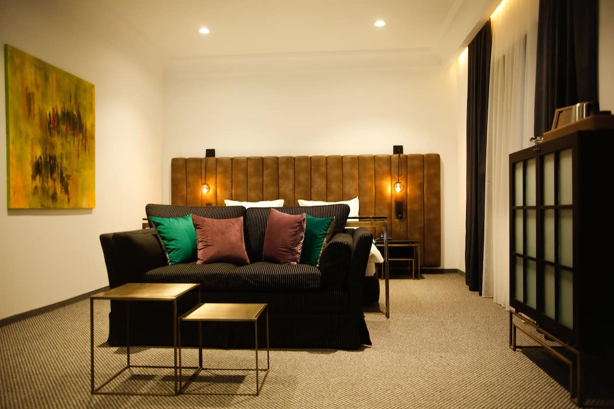 A modern hotel room with a sectional sofa, a small table, a cabinet, and a painting on the wall.