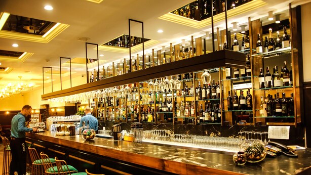 Una zona de bar con una barra larga, varias estanterías llenas de botellas y taburetes de bar.