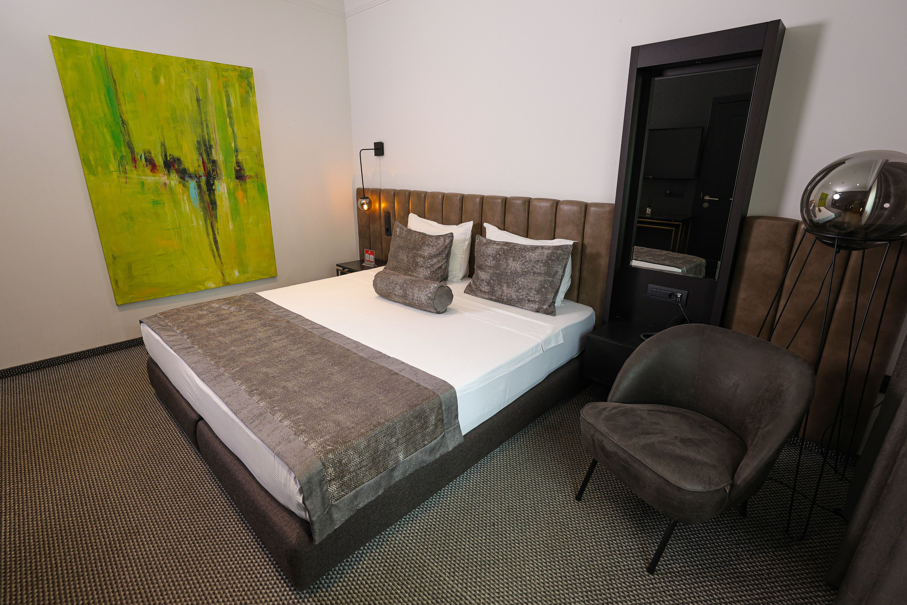 Ein Hotelzimmer mit Bett, Sessel, Nachttisch, Lampe und einem Bild an der Wand.