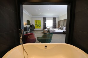 A modern hotel room with a large bathtub, a bed, a desk, and a chair. - Hotel Rubis (Ferizaj)