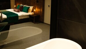 Un baño moderno con una bañera independiente, una cama con almohadas verdes y marrones, y una mesita de noche pequeña.