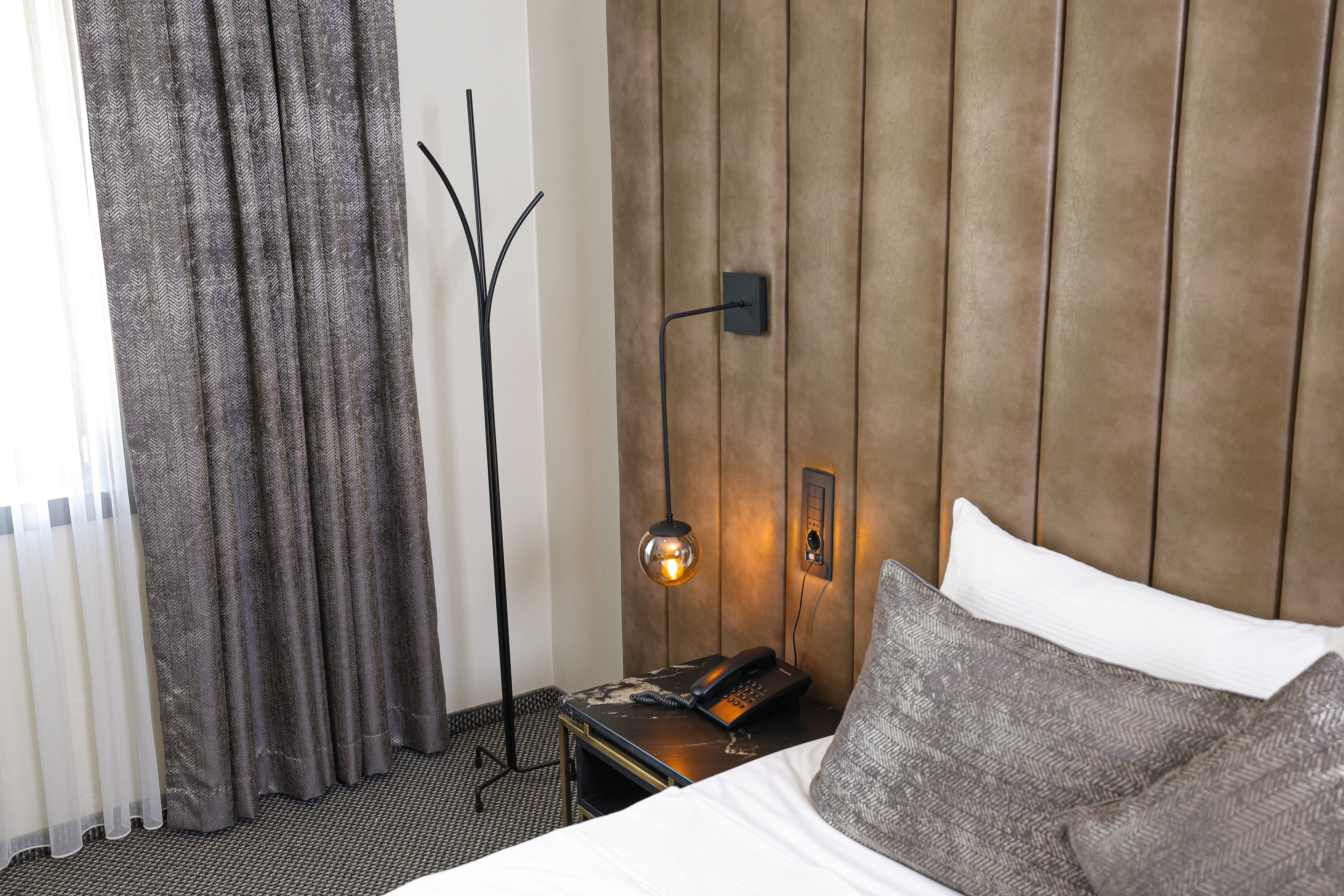 Habitación de hotel con cama, mesita de noche con teléfono, luz empotrada en la pared y lámpara de pie.