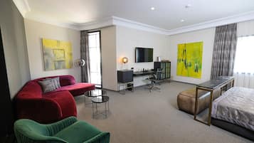 Een hotelkamer met een rode bank, een groene fauteuil, een bed, een bureau met stoel, een televisie en twee grote schilderijen.