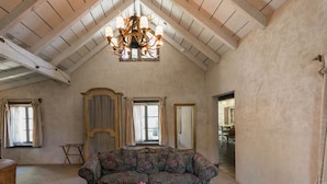 A spacious loft with a high ceiling, a floral sofa, a wooden coffee table, and a chandelier.