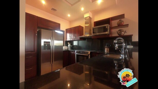 A modern kitchen with stainless steel appliances, wooden cabinets, and a black granite countertop. - "SLOW M’OCEAN VIEWS"  Golf Course & Resort (Roatan)