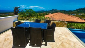A patio with a table and chairs overlooking a swimming pool and a scenic view of hills and the ocean. - "SLOW M’OCEAN VIEWS"  Golf Course & Resort (Roatan)