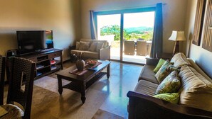 A living room with a TV, sofa, and a view of the outdoors. - "SLOW M’OCEAN VIEWS"  Golf Course & Resort (Roatan)