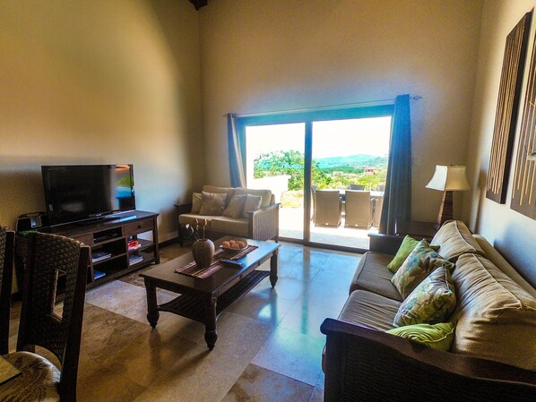 A living room with a TV, sofa, and a view of the outdoors.