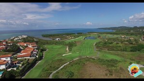 A golf course with a view of the ocean and residential buildings. - "SLOW M’OCEAN VIEWS"  Golf Course & Resort (Roatan)