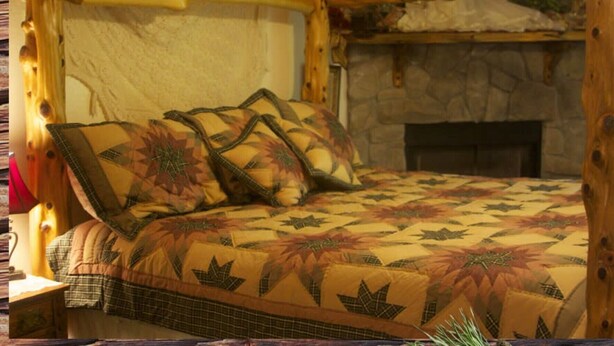 Een bed met een bloemenprint deken en kussens, een stenen open haard en houten balken.
