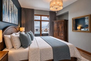 A bedroom with a large bed, a wardrobe, a chandelier, and a view of a snowy landscape.