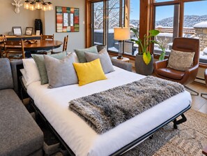 Un dormitorio con cama, una silla, una mesa y un ventanal con vistas a un paisaje nevado.