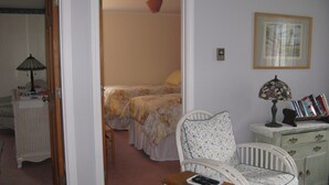 A bedroom with two beds, a chair, a nightstand, a lamp, and a dresser.